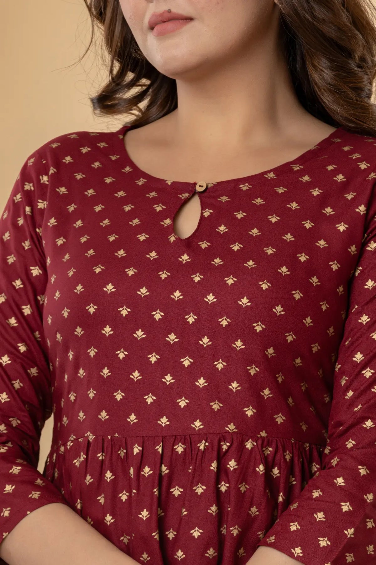 Maroon dress with gold floral pattern worn by a person against a beige background