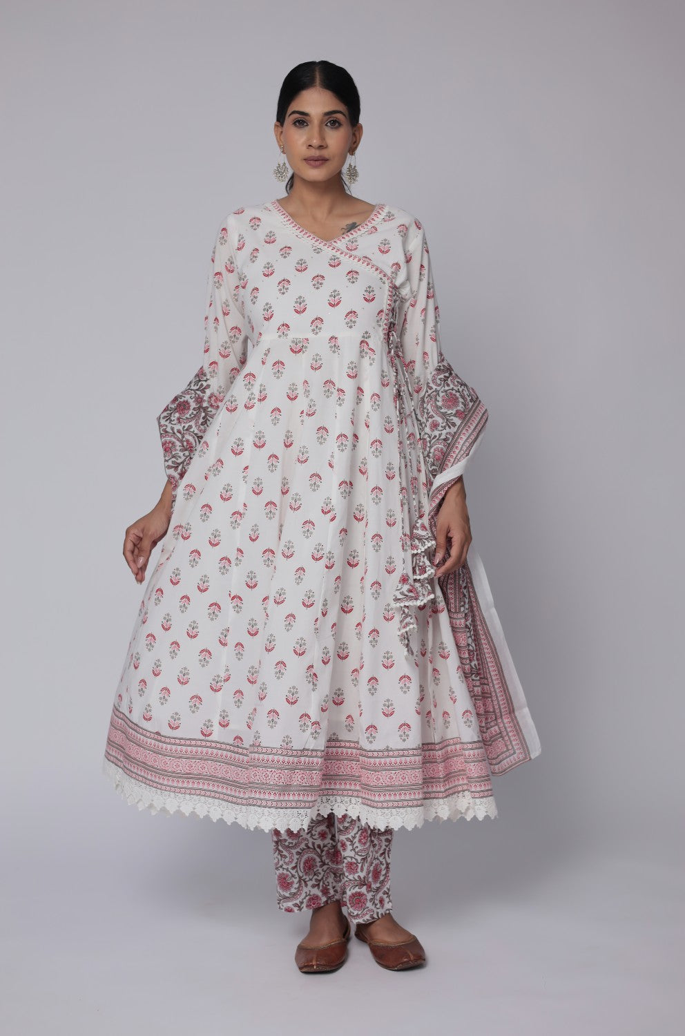 Model wearing an artisan crafted white and red cotton Anarkali set from The Navra, featuring a Jaipuri print kurta, handwork on the neck, crochet lace details, and a matching printed dupatta. Ideal for comfortable ethnic wear.