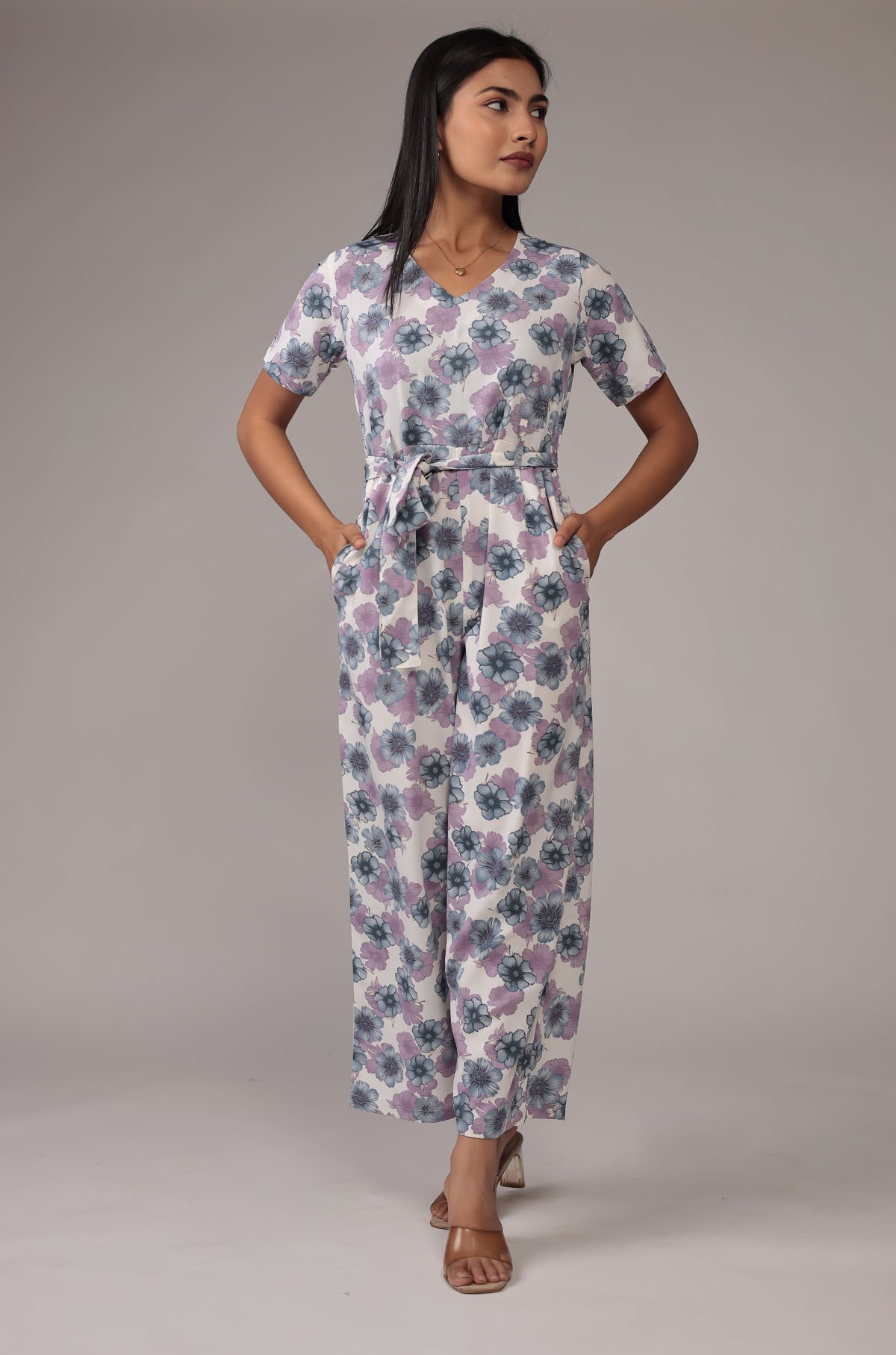 Model wearing a beautiful white floral print co-ord set from The Navra, featuring pastel purple and green patterns, a V-neck top with short sleeves and a tie-up waist, and matching wide-leg pants. Ideal for casual or everyday comfort.