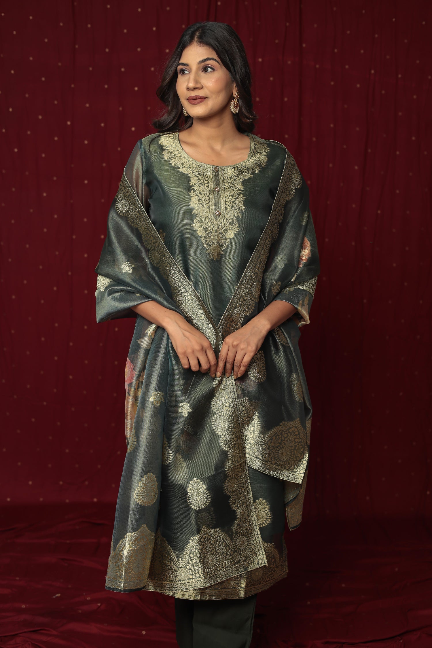 Model wearing a deluxe dark green jacquard suit from The Navra, featuring intricate gold woven patterns on the kurti and matching jacquard dupatta, paired with soft silk pants. Perfect for festive occasions.
