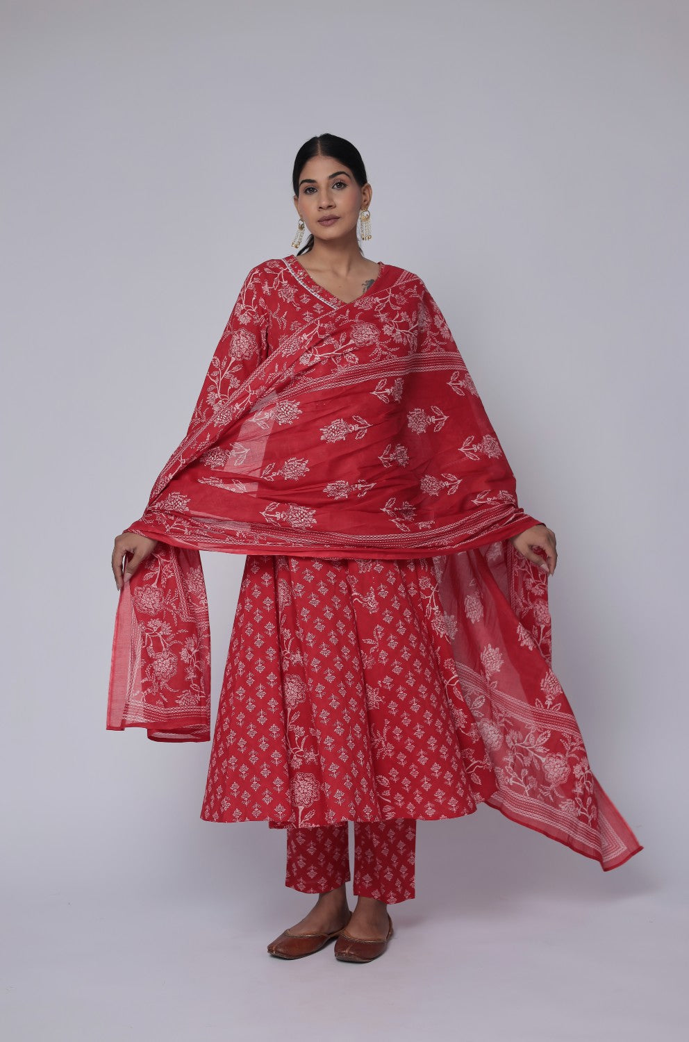 Model wearing a vibrant red cotton Anarkali dupatta set from The Navra, featuring intricate white handwork on the neck, a flowing Jaipuri printed kurta, and a matching printed dupatta. Ideal for comfortable daily or festive ethnic wear.