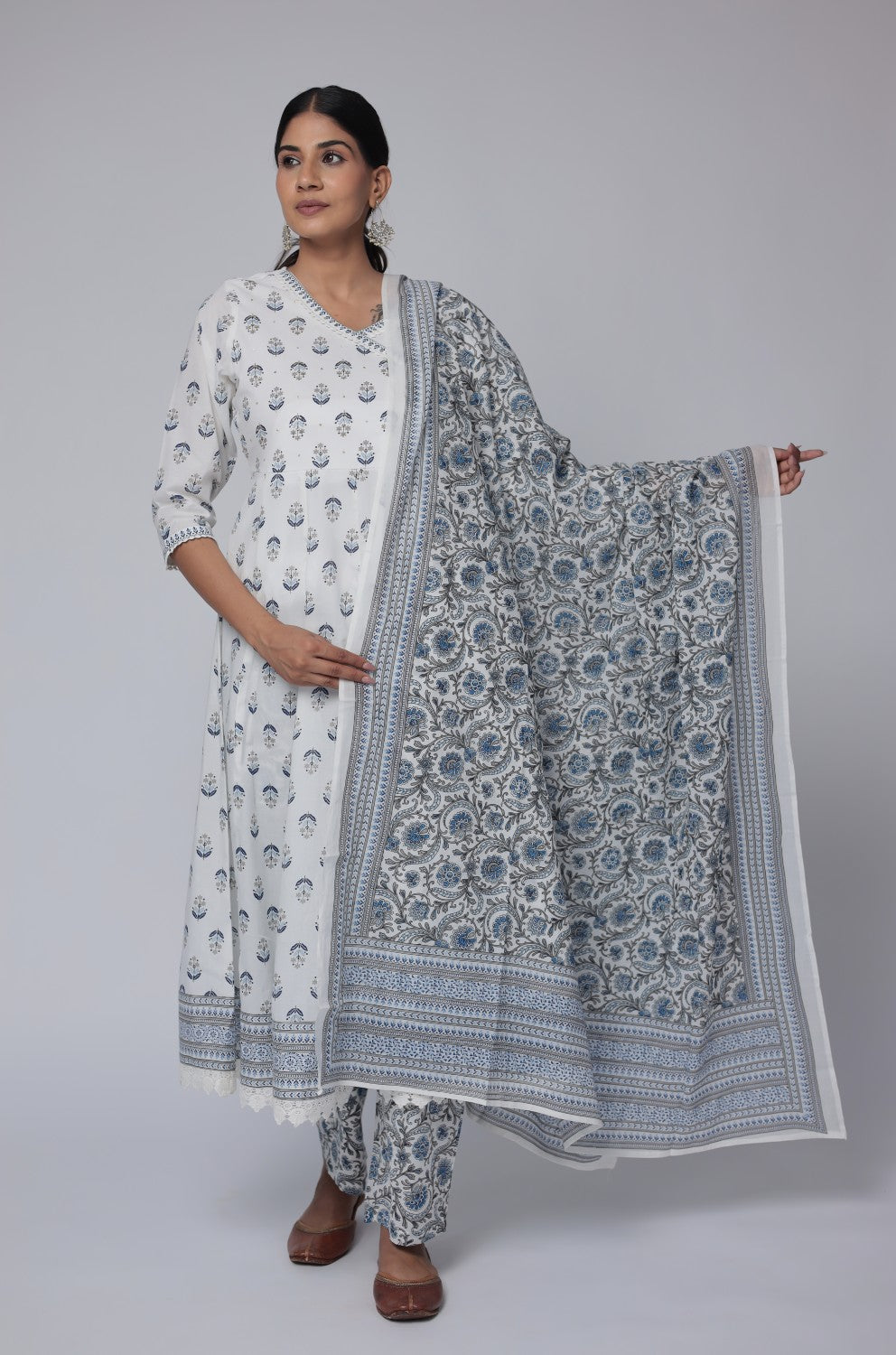 Model wearing a vibrant white and blue cotton Anarkali dupatta set from The Navra, featuring intricate handwork on the neck, a flowing Jaipuri print kurta with crochet lace, and a matching printed dupatta. Ideal for comfortable daily or festive ethnic wear.