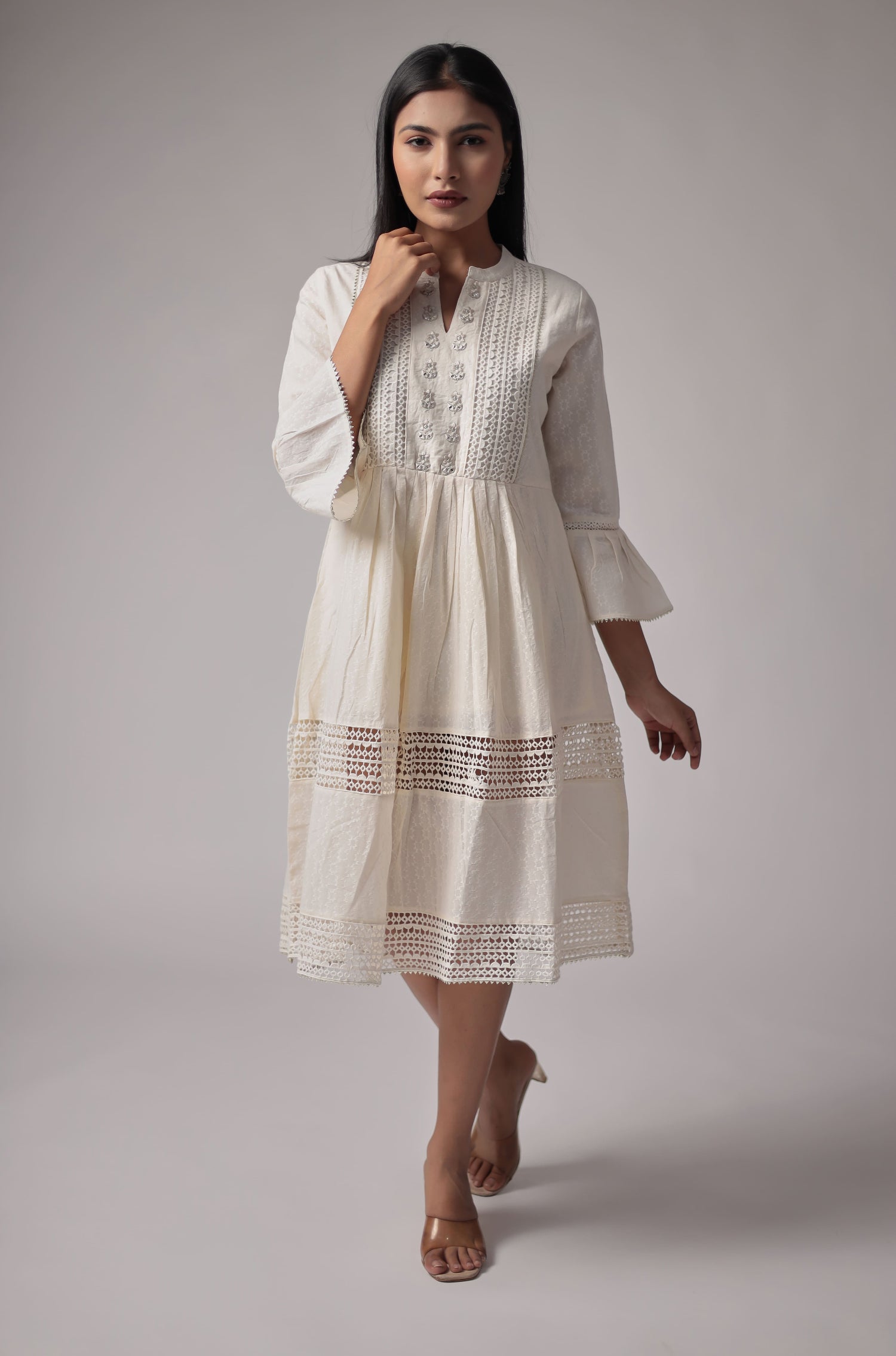 Model walking in a beautiful white cotton dobby dress from The Navra, featuring intricate neck embroidery, premium crochet fabric detailing, and elegant bell sleeves. Ideal for comfortable casual or festive wear.