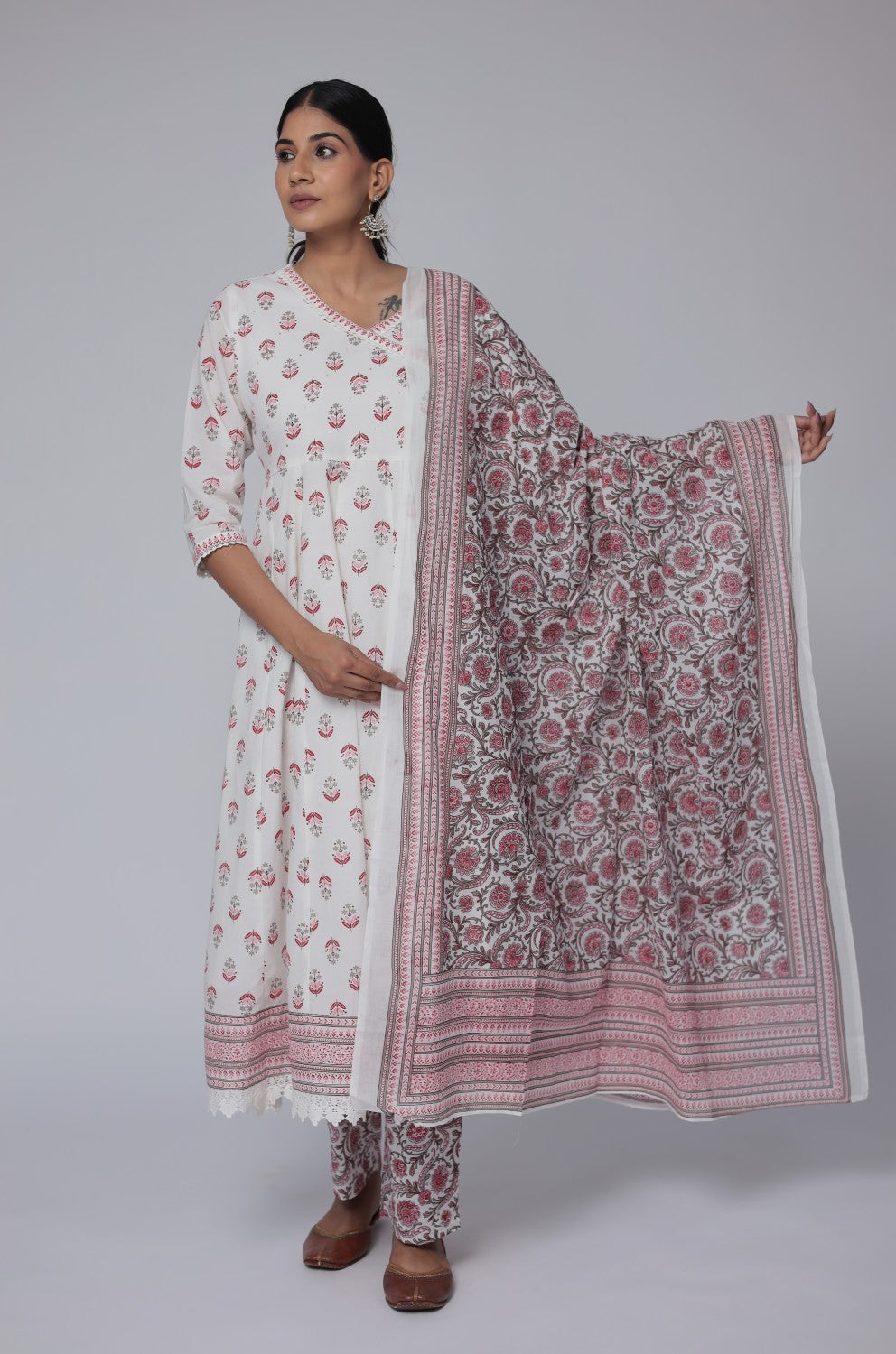 Woman wearing a white kurta with pink floral patterns, holding a matching dupatta on a gray background
