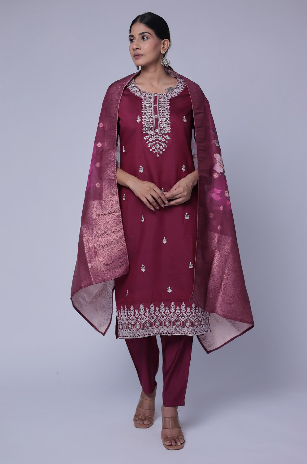 Model wearing a luxurious wine soft silk suit set from The Navra, featuring exquisite white thread embroidery and sequins on the kurti, and a beautiful printed jacquard dupatta. Paired with comfortable matching pants, ideal for festive or formal occasions.