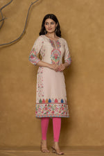 Model wearing a beige pannel kurta from The Navra, featuring colorful intricate handwork on the round neck and floral patterns along the hemline, paired with bright pink leggings. Ideal for casual and daily ethnic wear.