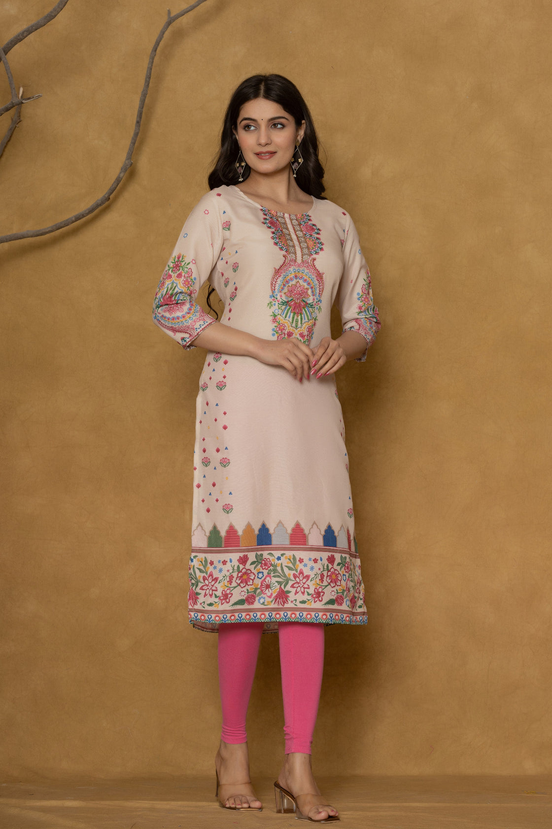 Model wearing a beige pannel kurta from The Navra, featuring colorful intricate handwork on the round neck and floral patterns along the hemline, paired with bright pink leggings. Ideal for casual and daily ethnic wear.