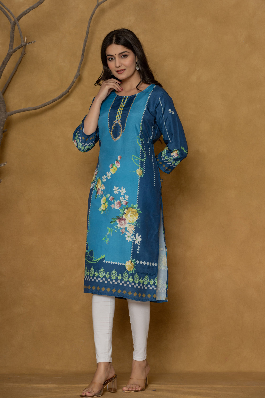 Model wearing a vibrant blue kurta from The Navra, intricately detailed with handwork on the round neck, featuring colorful floral prints, paired with white leggings. Ideal for comfortable daily or casual ethnic wear.