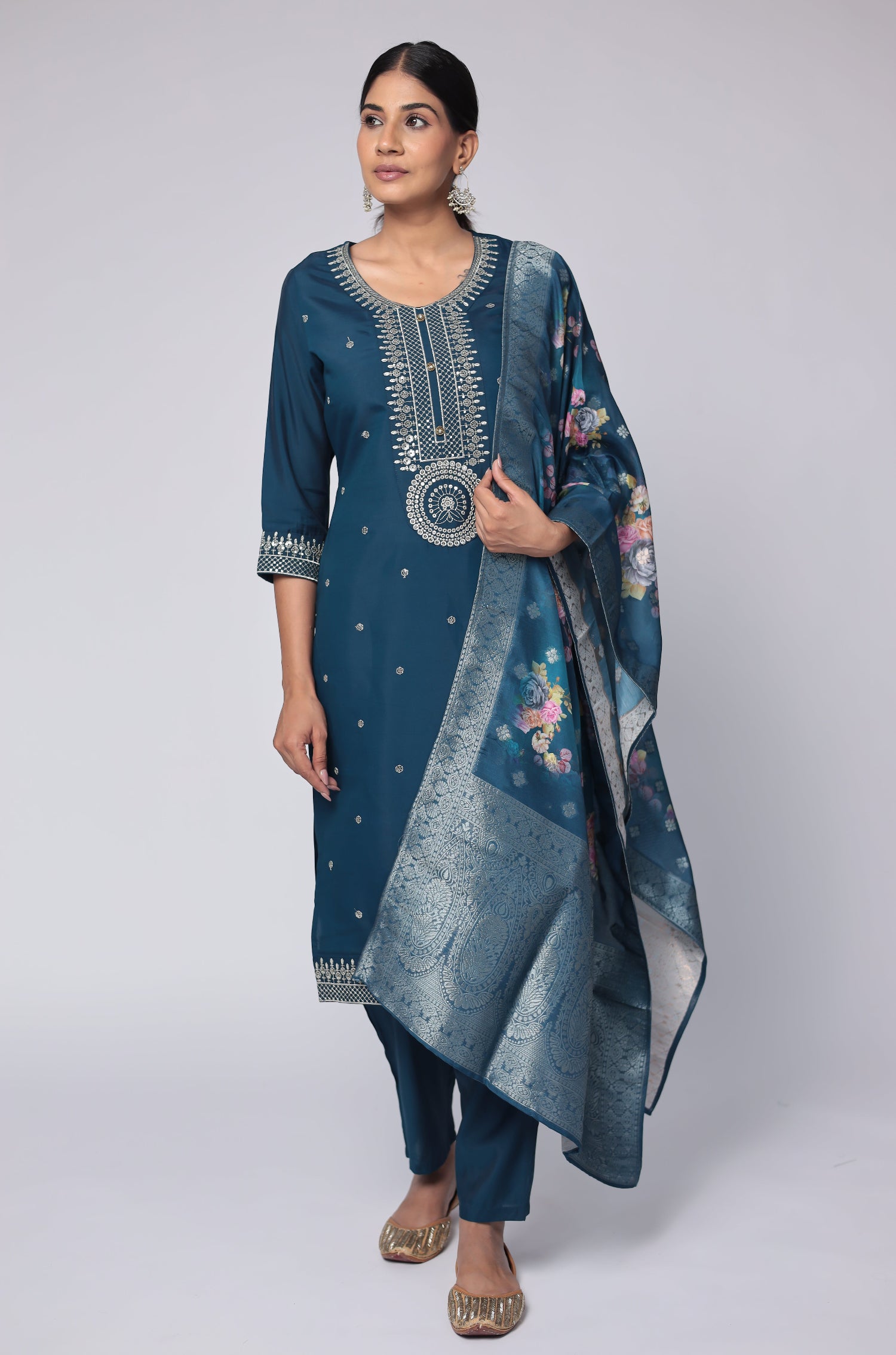 Model wearing a luxurious blue soft silk suit set from The Navra, featuring exquisite white thread embroidery and sequins on the kurti, and a beautiful printed jacquard dupatta. Paired with comfortable matching pants, ideal for festive or formal occasions.
