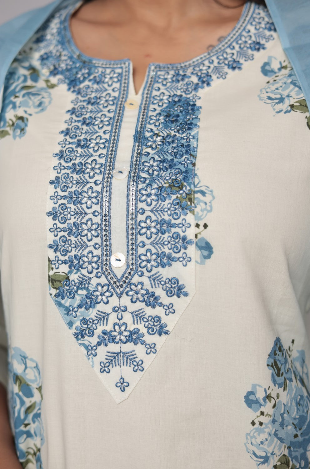 lose-up of the delicate neck embroidery and vibrant blue floral Jaipuri print on the cream kurta, highlighting intricate details.