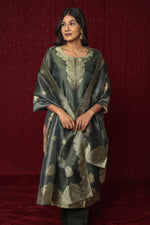 Model wearing a deluxe dark green jacquard suit from The Navra, featuring intricate gold woven patterns on the kurti and matching jacquard dupatta, paired with soft silk pants. Perfect for festive occasions.