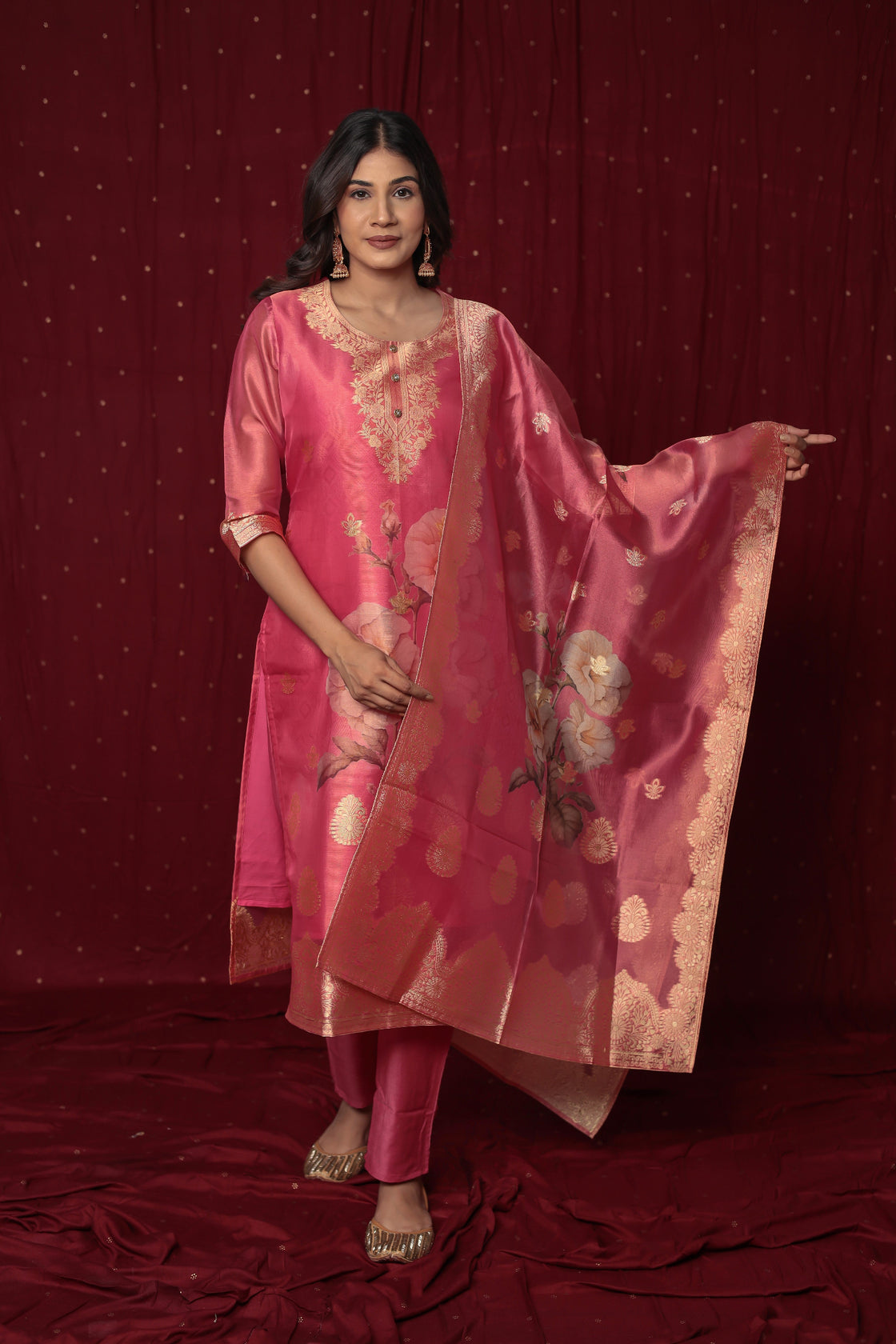Model wearing deluxe jacquard organza pink suit from The Navra, featuring shimmering gold woven patterns, embroidered kurti, and a grand jacquard dupatta, with soft silk pants. Ideal for festive occasions.