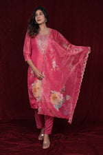 Model wearing deluxe shimmer organza pink suit from The Navra, featuring an embroidered kurti and elegant floral embroidered dupatta, with soft muslin pants. Ideal for festive occasions.