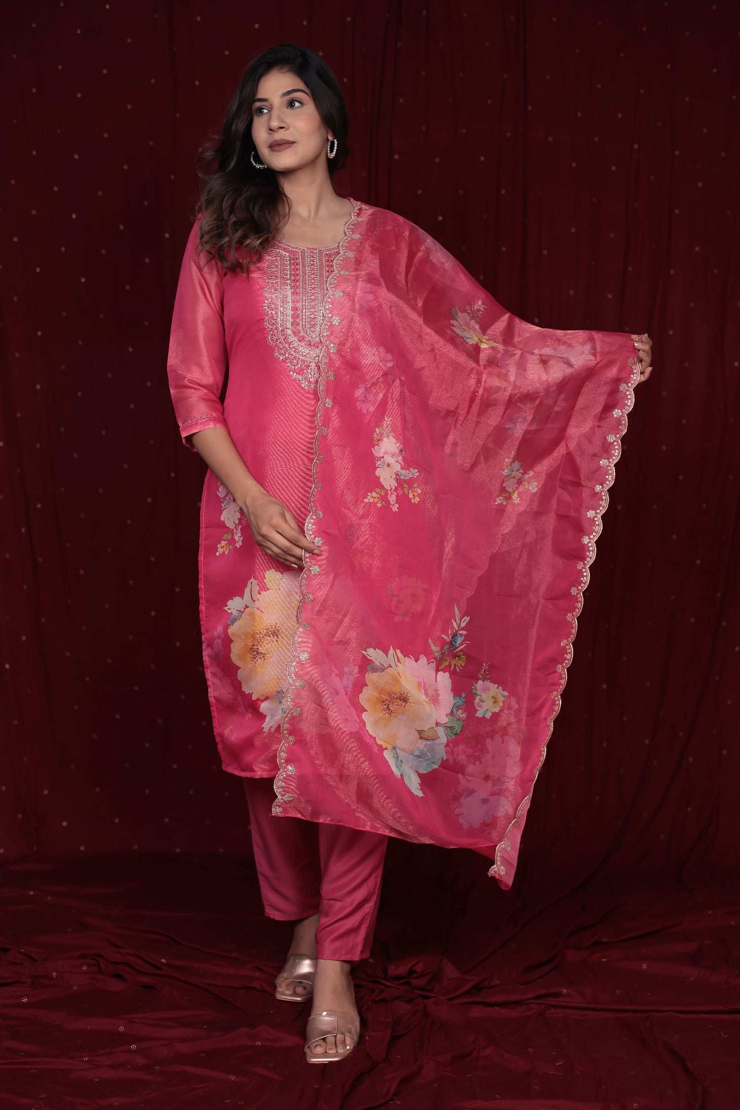 Model wearing deluxe shimmer organza pink suit from The Navra, featuring an embroidered kurti and elegant floral embroidered dupatta, with soft muslin pants. Ideal for festive occasions.