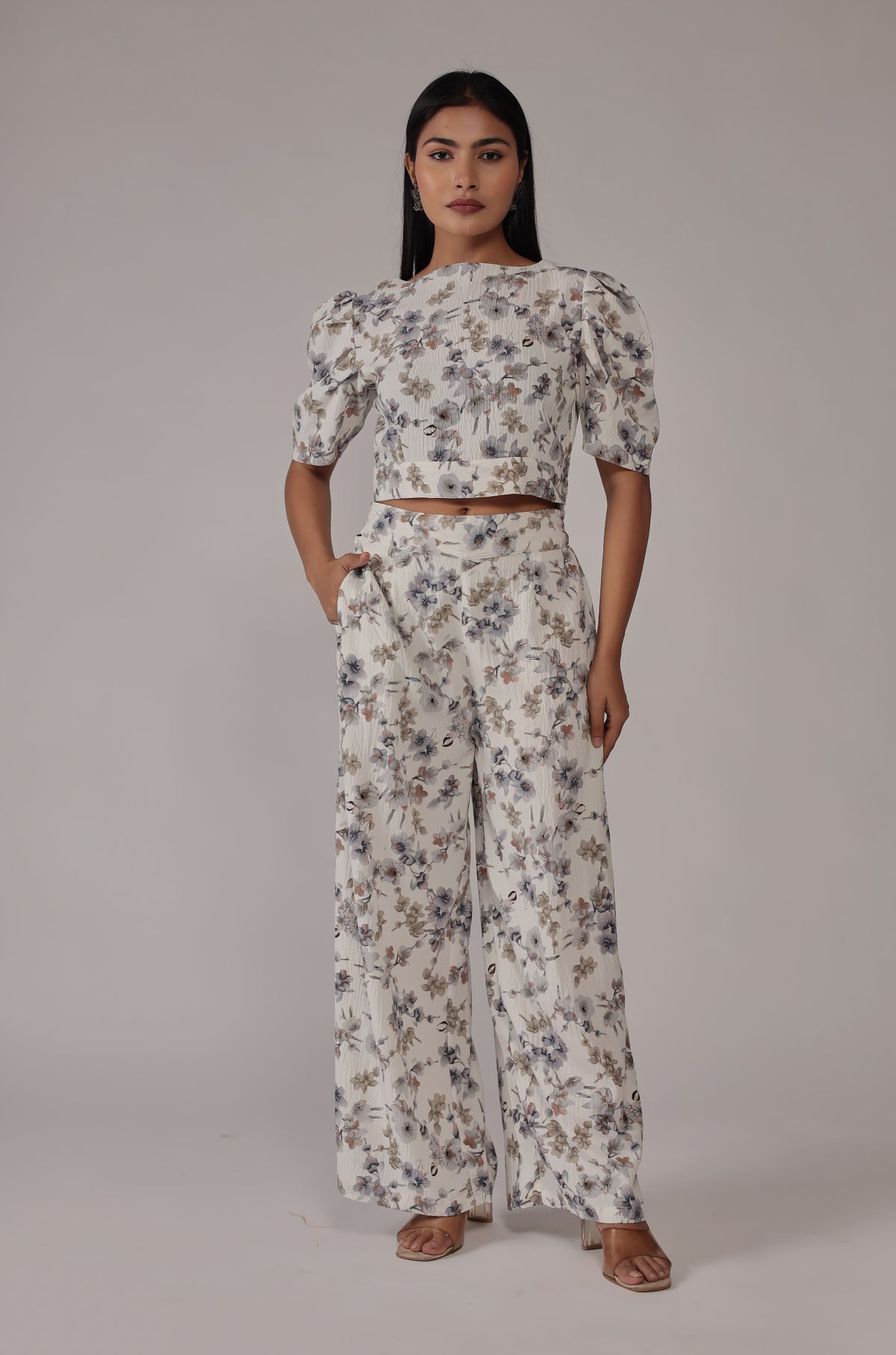Model wearing an elegant cream printed co-ord set from The Navra, featuring delicate blue and green floral patterns on a puff-sleeve crop top and matching wide-leg pants. Ideal for comfortable yet chic casual wear.