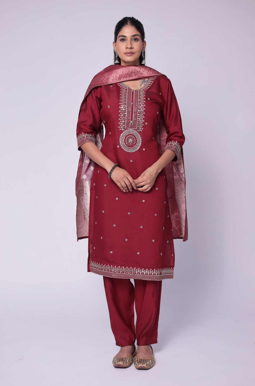 Model wearing a luxurious maroon soft silk suit set from The Navra, featuring exquisite white thread embroidery and sequins on the kurti, and a beautiful printed jacquard dupatta. Paired with comfortable matching pants, ideal for festive or formal occasions.
