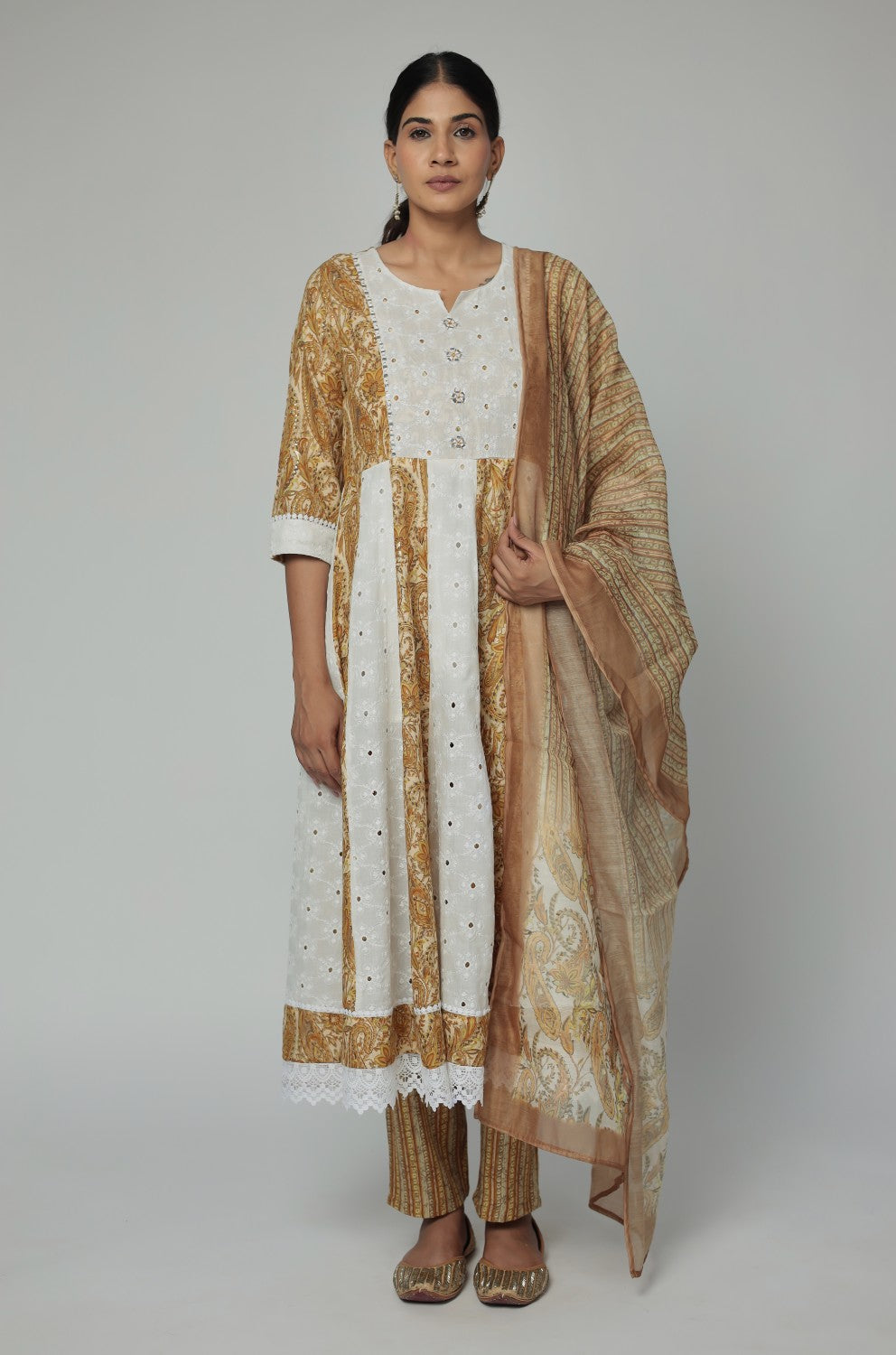 Model wearing a vibrant mustard yellow and white Schiffli Anarkali dupatta set from The Navra, featuring intricate mirror work, printed panels, and a matching sheer dupatta. Ideal for comfortable festive or semi-formal occasions.