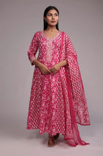 Model wearing a vibrant printed pink Anarkali dupatta set from The Navra, featuring intricate embroidery on the neck and sleeves, a flowing Anarkali kurta, and a matching printed dupatta. Ideal for festive or celebratory occasions.