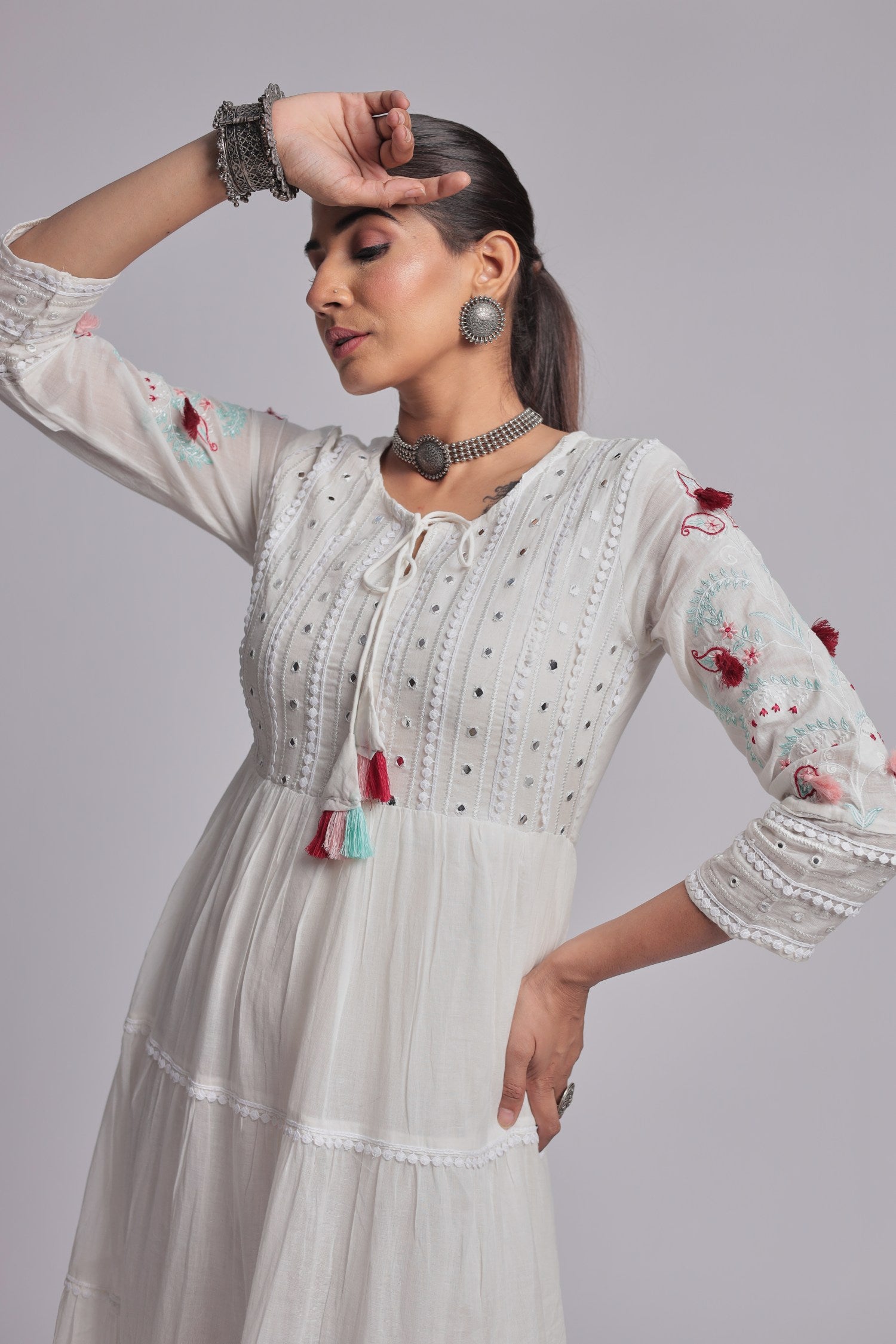 Model in a confident stance, highlighting the full length and comfortable design of the white tiered Anarkali dress with colorful tassels.