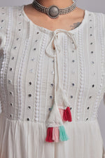 Close-up of the delicate white embroidery, dark embellishments, and colorful pink, blue, and orange tassels on the V-neckline of the white tiered Anarkali dress.