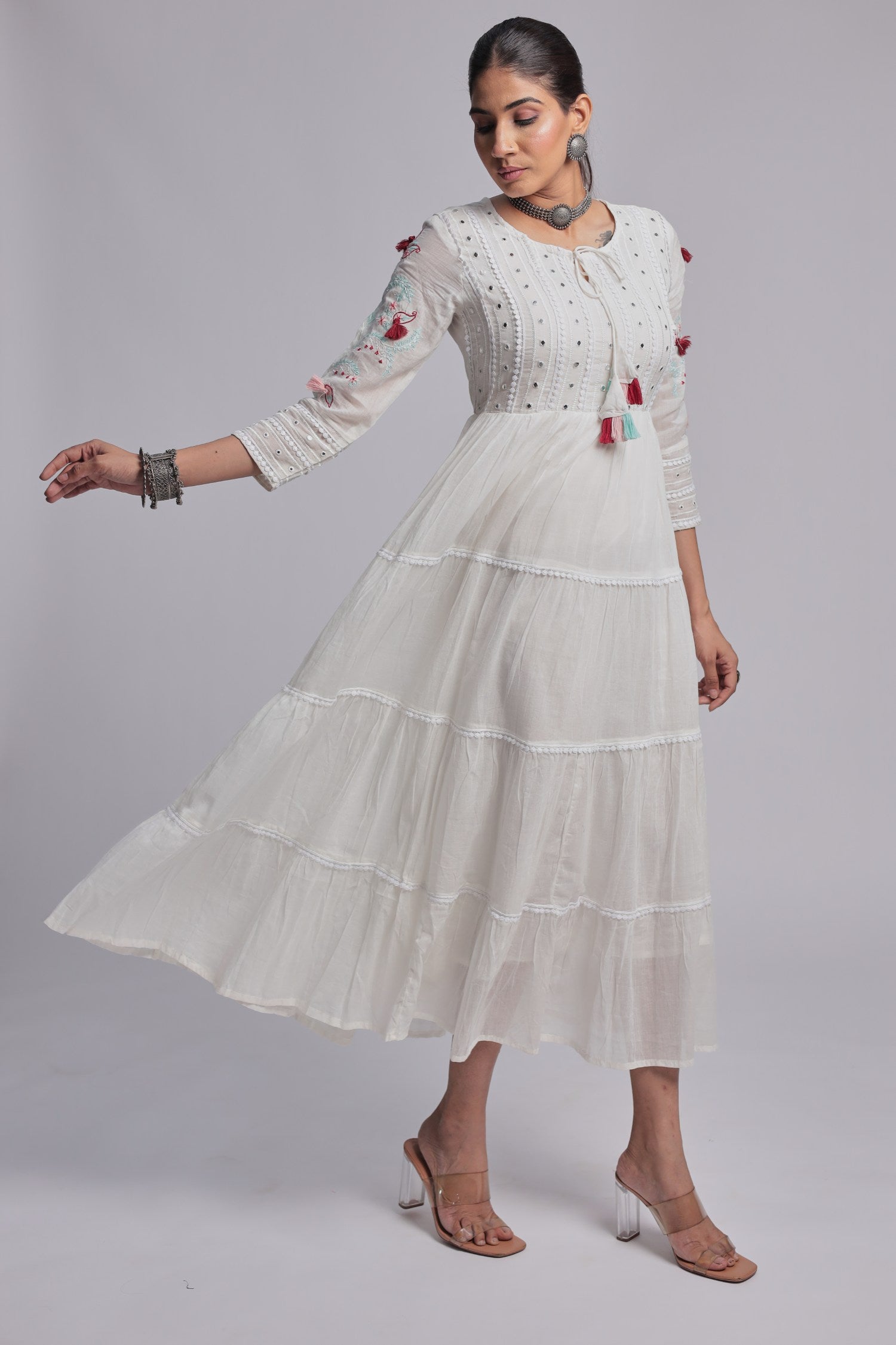 Side profile of model showcasing the voluminous tiered flare and comfortable movement of the white Anarkali dress with colorful tassels.